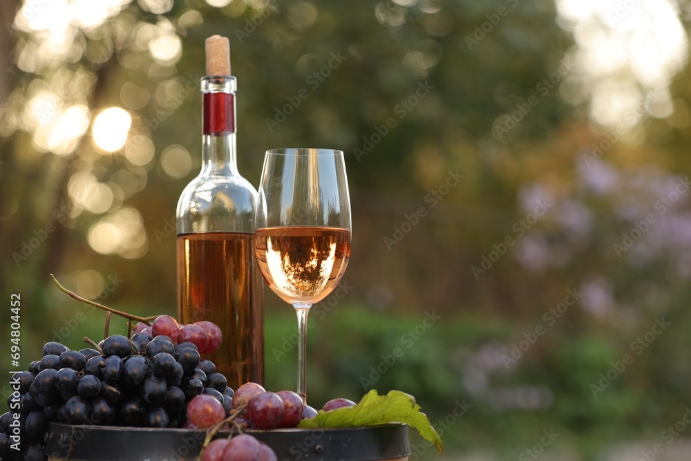 Delicious wine and ripe grapes on wooden barrel outdoors, space for text