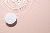 Cotton pad in micellar water on beige background, top view. Space for text