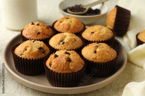 Delicious sweet muffins with chocolate chips on light textured table, closeup