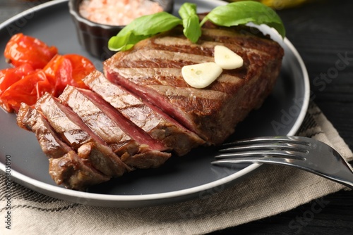 Delicious grilled beef steak served with spices and tomatoes on table, closeup