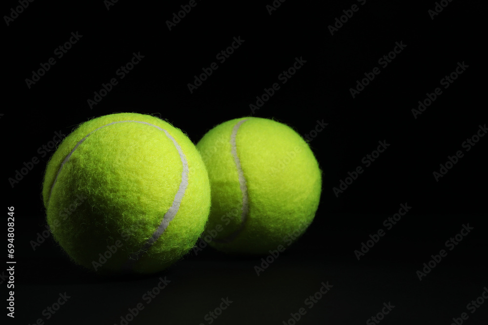 Two tennis balls on black background, closeup. Space for text
