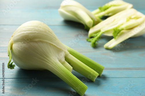 Whole and cut fennel bulb on light blue wooden table, closeup