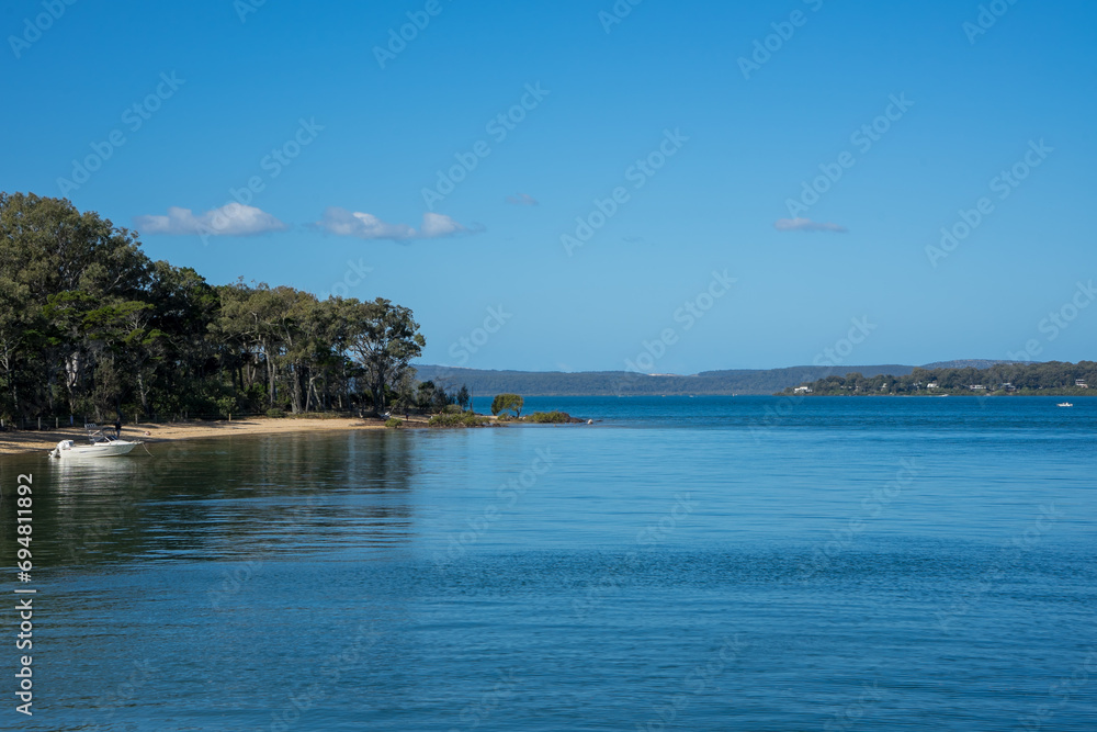 View across calm water to the sandy shore of Coochiemudlo Island, with Macleay Island and Stradbroke Island in the distance.