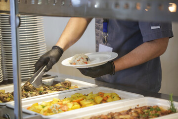 Buffet style service - Canteen worker at serving line putting food on the plate	