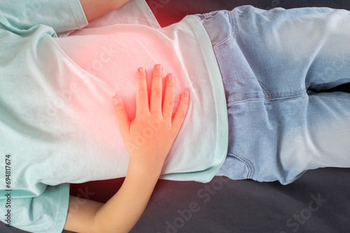 Fotografía A seven-year-old girl in a green T-shirt lies and holds her sore stomach with her hands