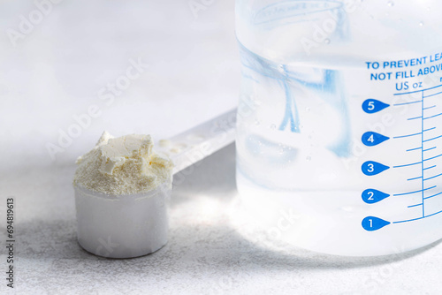 A baby feeding bottle and a measuring spoon with a handful of dry baby formula for preparing milk for the baby. Useful and healthy food, close-up photo