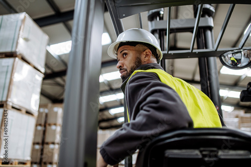 Multiracial warehouse worker driving forklift. Warehouse worker preparing products for shipmennt, delivery, checking stock in warehouse.