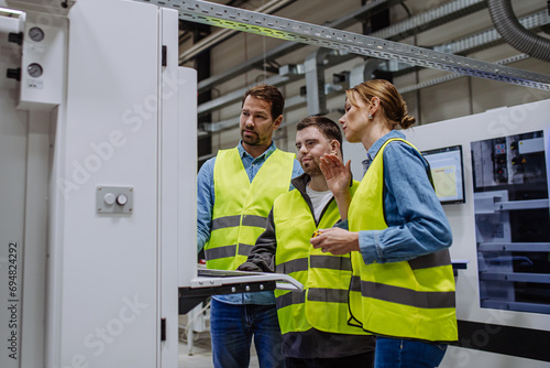 Young man with Down syndrome working in warehouse, colleague teaching him work with computer. Concept of workers with disabilities, support in workplace.