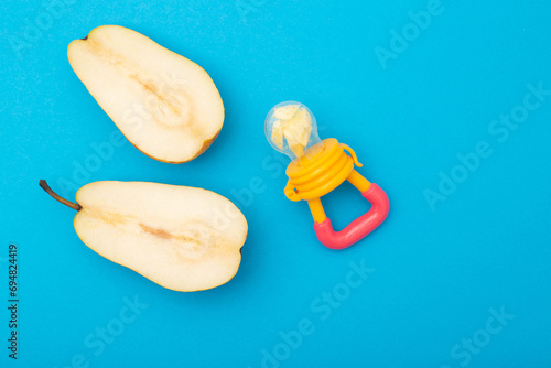 A pear cut in half on a blue background and a baby nibbler for feeding babies. Concept of the benefits of fruits and vitamins for babies. Copy space for text photo