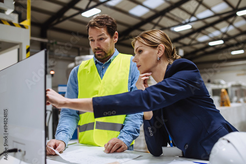 Female engineer reading technical documentation with project manager in modern industrial factory, talking about new production project, investment. Team management in manufacturing facility.