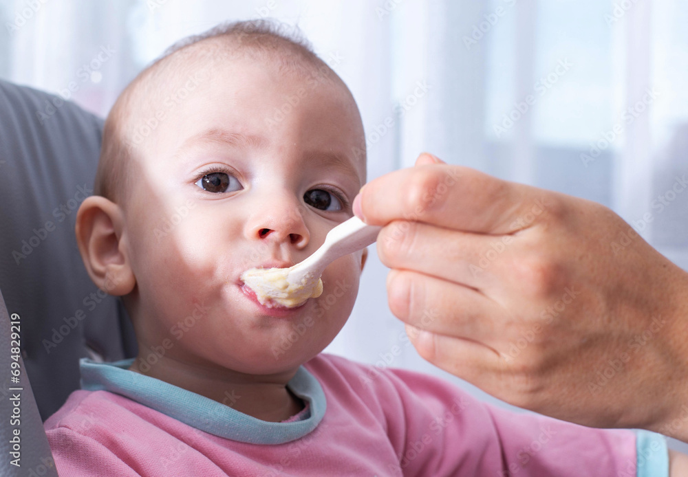 A mother feeds her caucasian child, a one-year-old boy, with millet porridge. Feeding children dairy-free and gluten-free porridge with vitamins and macroelements, close-up. Copy space for text A mother feeds her caucasian child, a one-year-old boy, with millet porridge. Feeding children dairy-free and gluten-free porridge with vitamins and macroelements, close-up. Copy space for text
