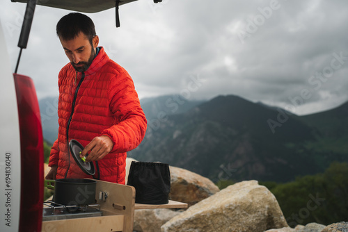 Man in winter jacker cooking food during hiking in countryside photo