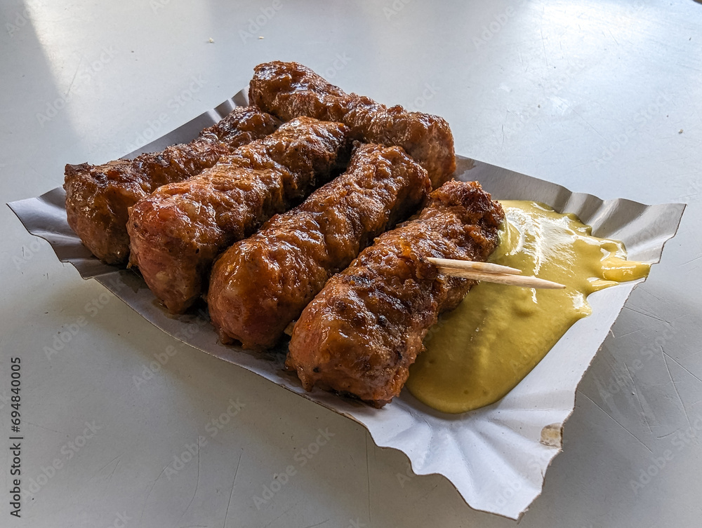 Mici with mustard and a toothpick on a paper plate. Traditional romanian fast food.