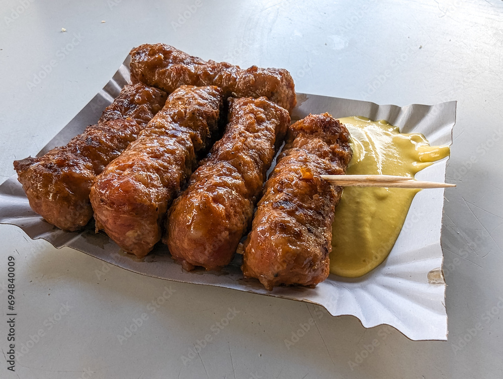 Mici with mustard and a toothpick on a paper plate. Traditional romanian fast food.