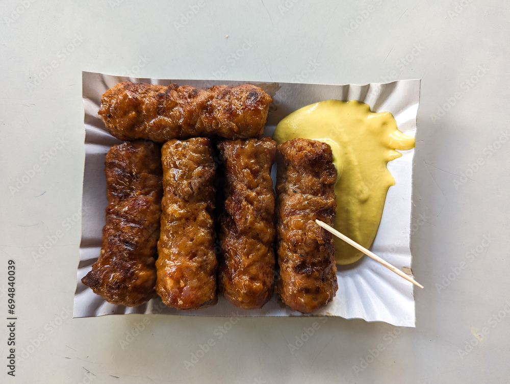 Mici with mustard and a toothpick on a paper plate. Traditional romanian fast food.