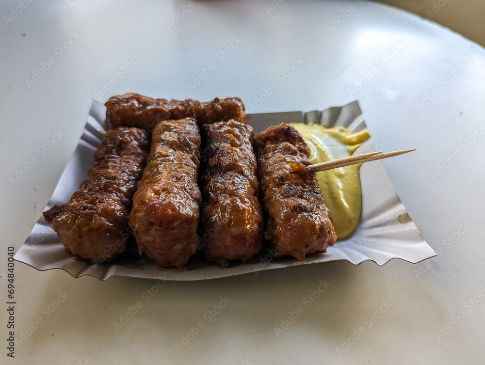 Mici with mustard and a toothpick on a paper plate. Traditional romanian fast food.
