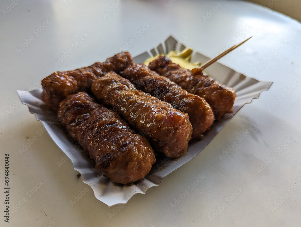 Mici with mustard and a toothpick on a paper plate. Traditional romanian fast food.