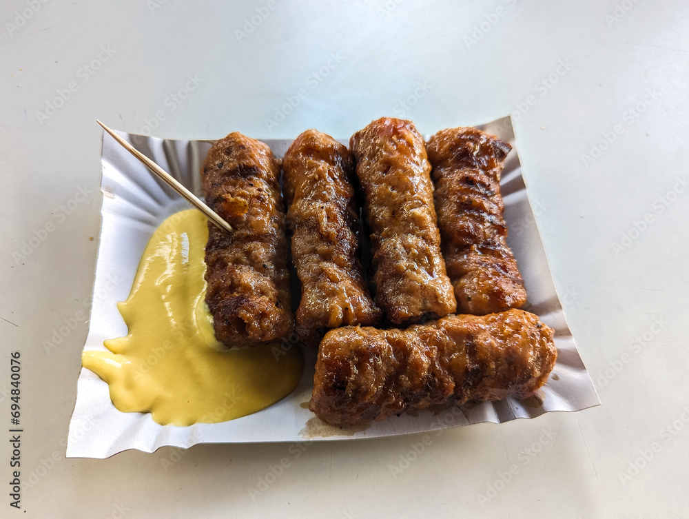 Mici with mustard and a toothpick on a paper plate. Traditional romanian fast food.
