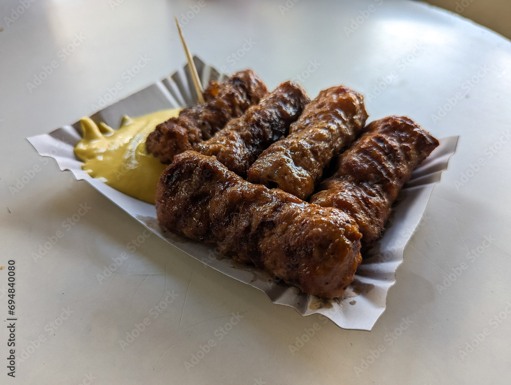 Mici with mustard and a toothpick on a paper plate. Traditional romanian fast food.