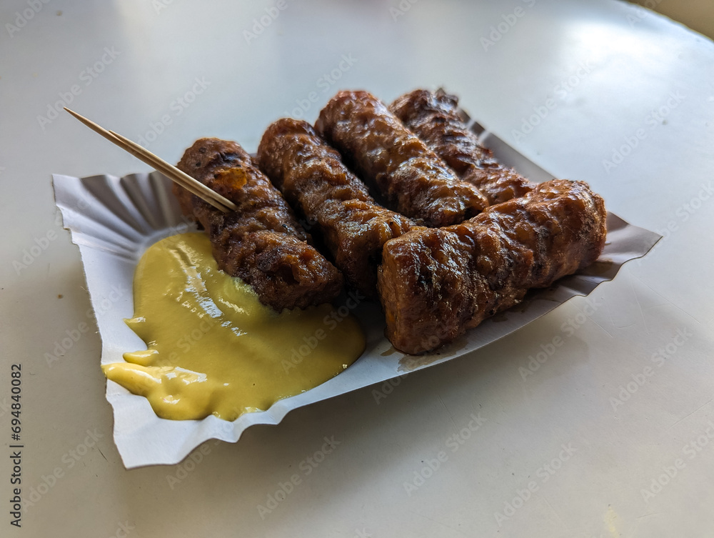 Mici with mustard and a toothpick on a paper plate. Traditional romanian fast food.