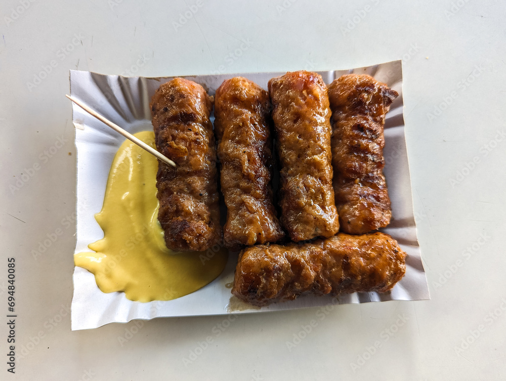 Mici with mustard and a toothpick on a paper plate. Traditional romanian fast food.