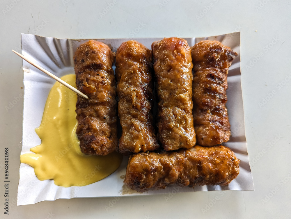 Mici with mustard and a toothpick on a paper plate. Traditional romanian fast food.