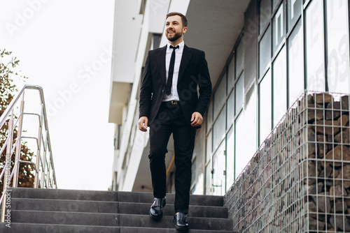 Handsome business man in black suit walking down the stairs by office center