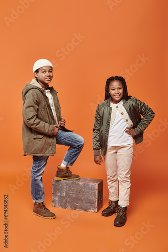 cheerful preteen african american friends in winter attires posing together on orange backdrop