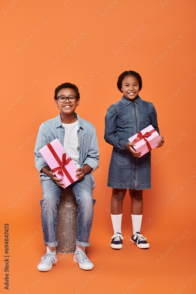 cheerful african american children holding wrapped presents and standing on orange background cheerful african american children holding wrapped presents and standing on orange background