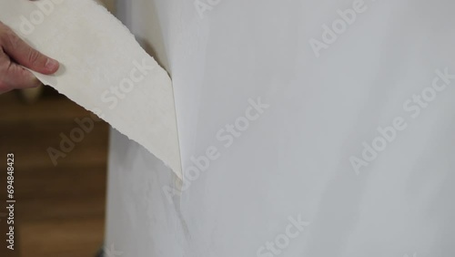 Caucasian man pulls with his hands and tears off piece of wallpaper from the wall. Close up of wall preparation during renovation by inexperienced person indoor.