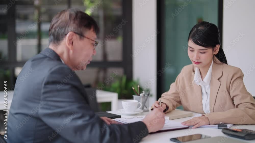 Young Asian businesswoman engaging in a focused conversation with a senior business colleague, both armed with determination, working in a modern office setting Young Asian businesswoman engaging in a focused conversation with a senior business colleague, both armed with determination, working in a modern office setting