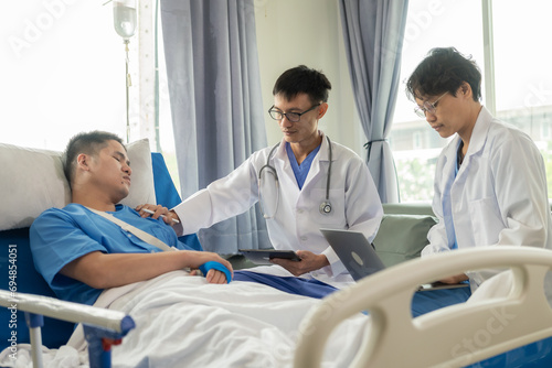 An Asian male patient lies in a hospital bed and is carefully looked after by a doctor. Doctor giving advice to male patient Working on health disease diagnosis © ArLawKa
