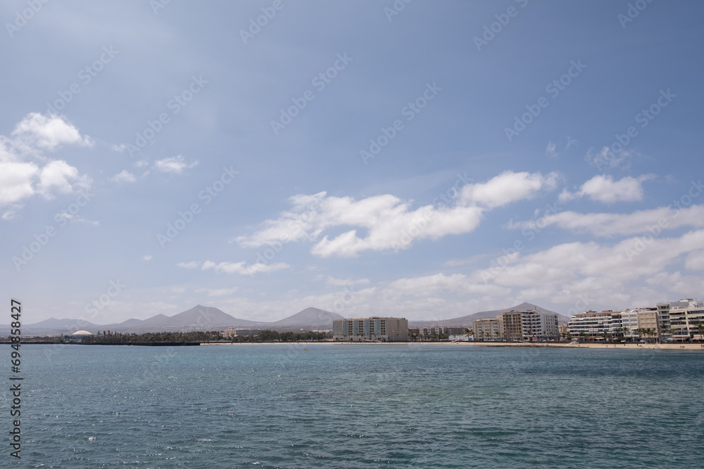 View of the Reducto beach and mountains in the background, from the Fermina islet. Turquoise blue water. Sky with big white clouds. Seascape. Lanzarote, Canary Islands, Spain.