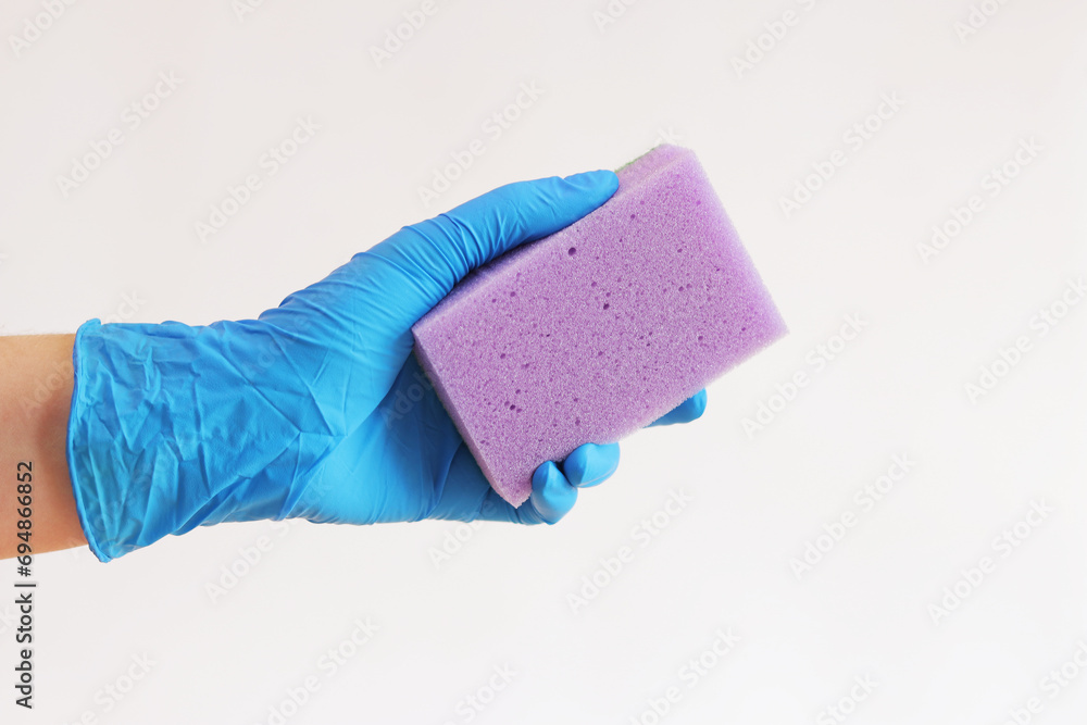 Sponge in hand, wet cleaning of the room, light background. A woman's hand in a latex blue glove with a purple sponge. Cleaning. Wash dishes Sponge in hand, wet cleaning of the room, light background. A woman's hand in a latex blue glove with a purple sponge. Cleaning. Wash dishes