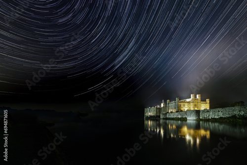 Leeds castle illuminated reflected in moat showing star trails in the night sky, near Maidstone, Kent, England photo