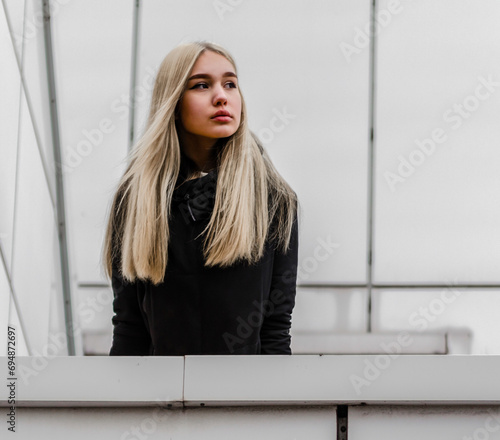 young girl with blond hair and black clothes against a gray building