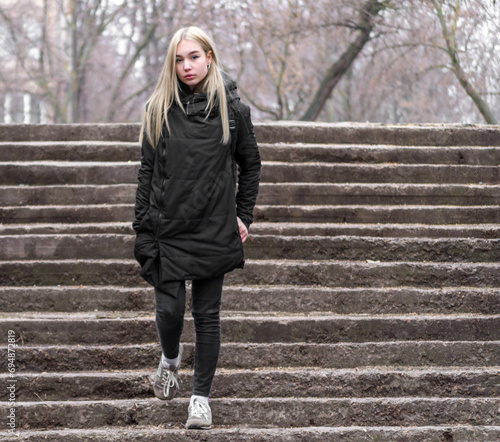 young girl with blond hair in black clothes comes down the stone stairs © Sofiia