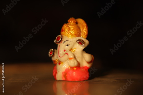 A colorful Small or miniature statue or figurine of a lord ganesha or ganpati with reflection and black isolated background, diagonal shot