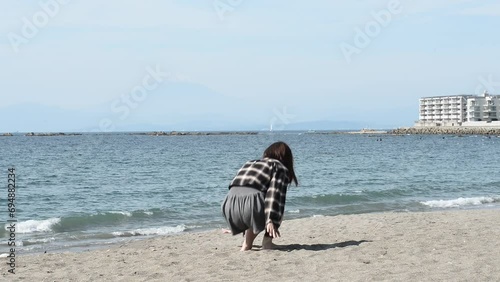 砂浜に座り立ち上がる若い女性