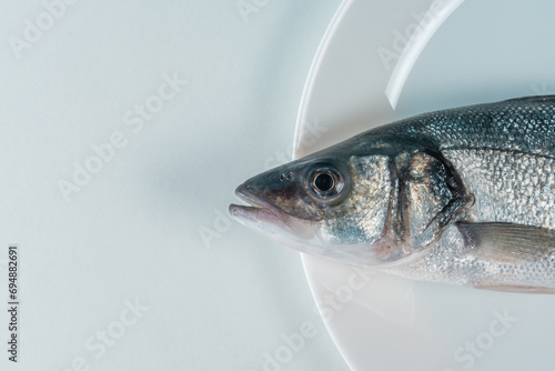 Raw fresh seabass fish on a white plate. Minimal food concept. Top view.