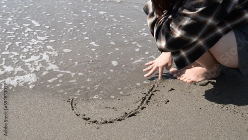 砂浜に書いたハートを波で消される女性