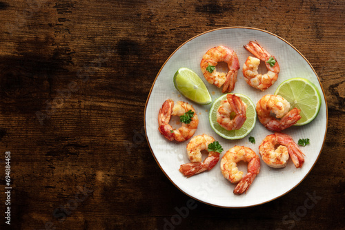 Shrimps, overhead flat lay shot with copy space. Fried shrimp with lime on a white plate, shot from the top on a rustic wooden background. Keto appetizer