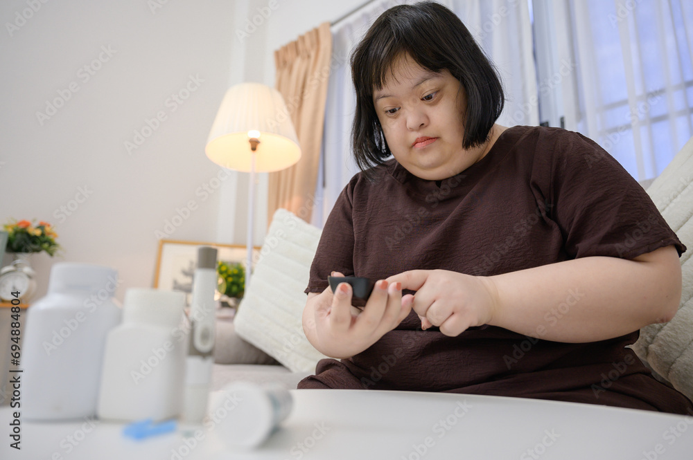 Asian fat woman who is disabled by Down syndrome A diabetic patient is looking at blood results on a blood sugar monitor with a blood sugar meter at home Asian fat woman who is disabled by Down syndrome A diabetic patient is looking at blood results on a blood sugar monitor with a blood sugar meter at home