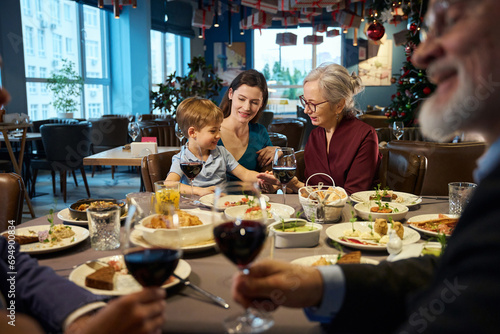 Happy senior woman sitting at table with little boy enjoying Thanksgiving dinner