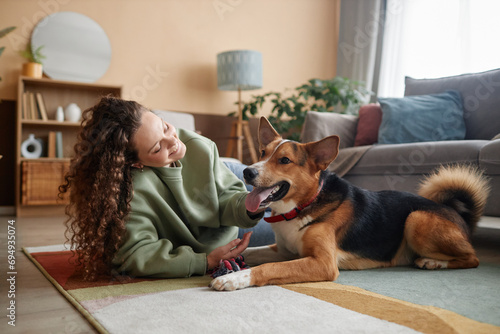 Full length portrait of happy young woman playing with big dog lying on floor in cozy home, copy space photo
