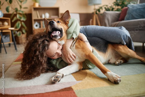 Portrait of young woman playing with happy dog fooling around on floor at home, copy space photo