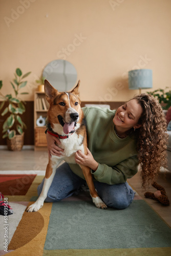Valokuva Vertical full length portrait of smiling young woman playing with mixed breed do