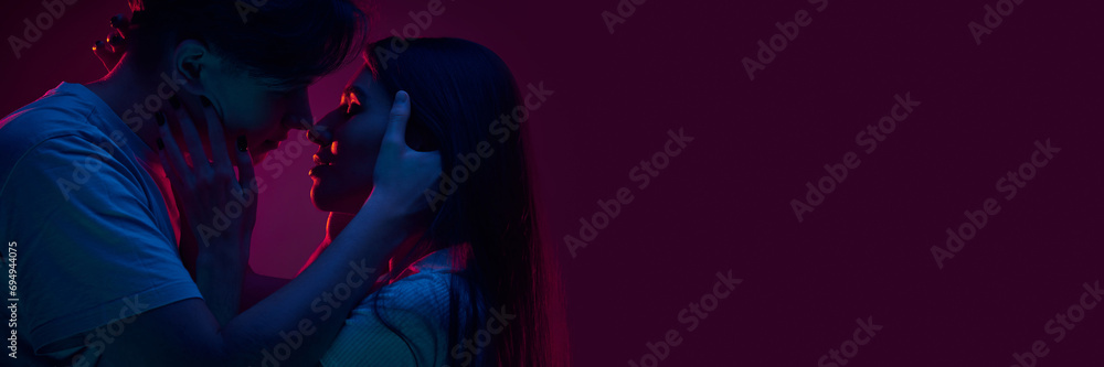 Portrait of young couple, boyfriend and girlfriend hugging and kissing, showing love against purple background in neon light. Concept of romance, love, relationship, passion, youth. Banner - obrazy, fototapety, plakaty 