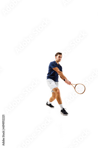 Full-length image of young man, tennis athlete in motion, playing, practicing isolated over white background. Concept of professional sport, competition, game, math, hobby, action