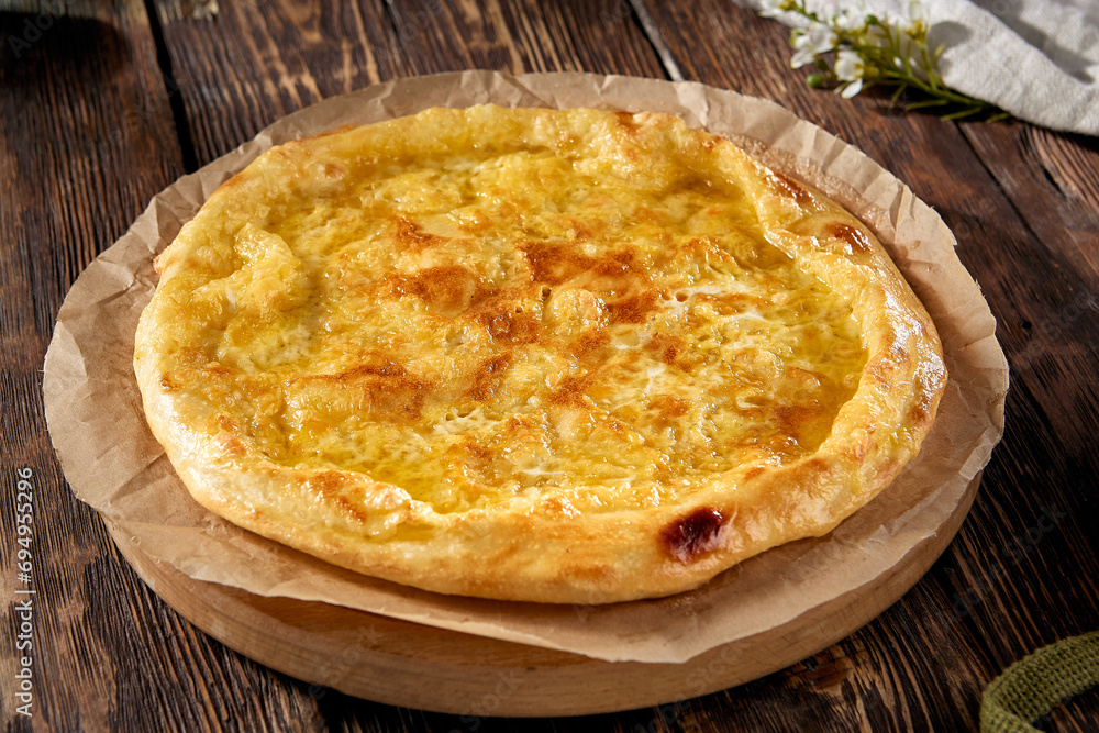 Golden-browned Megrelian khachapuri on parchment, with a rustic wooden backdrop, inviting and traditional Golden-browned Megrelian khachapuri on parchment, with a rustic wooden backdrop, inviting and traditional